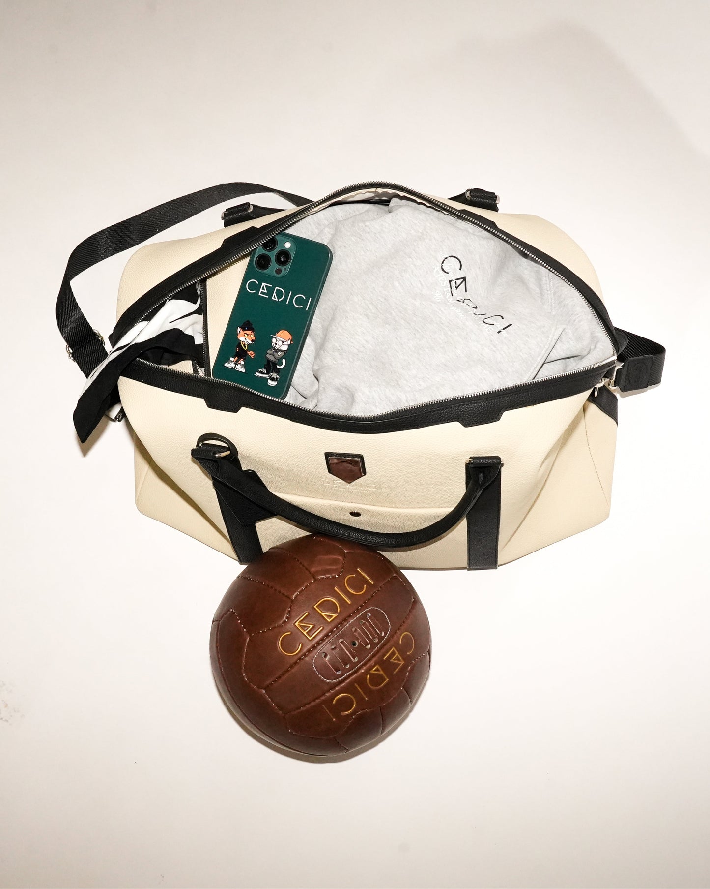 Beige bag with black handles and a brown leather ball labeled 'Cedici' on a light gray background.