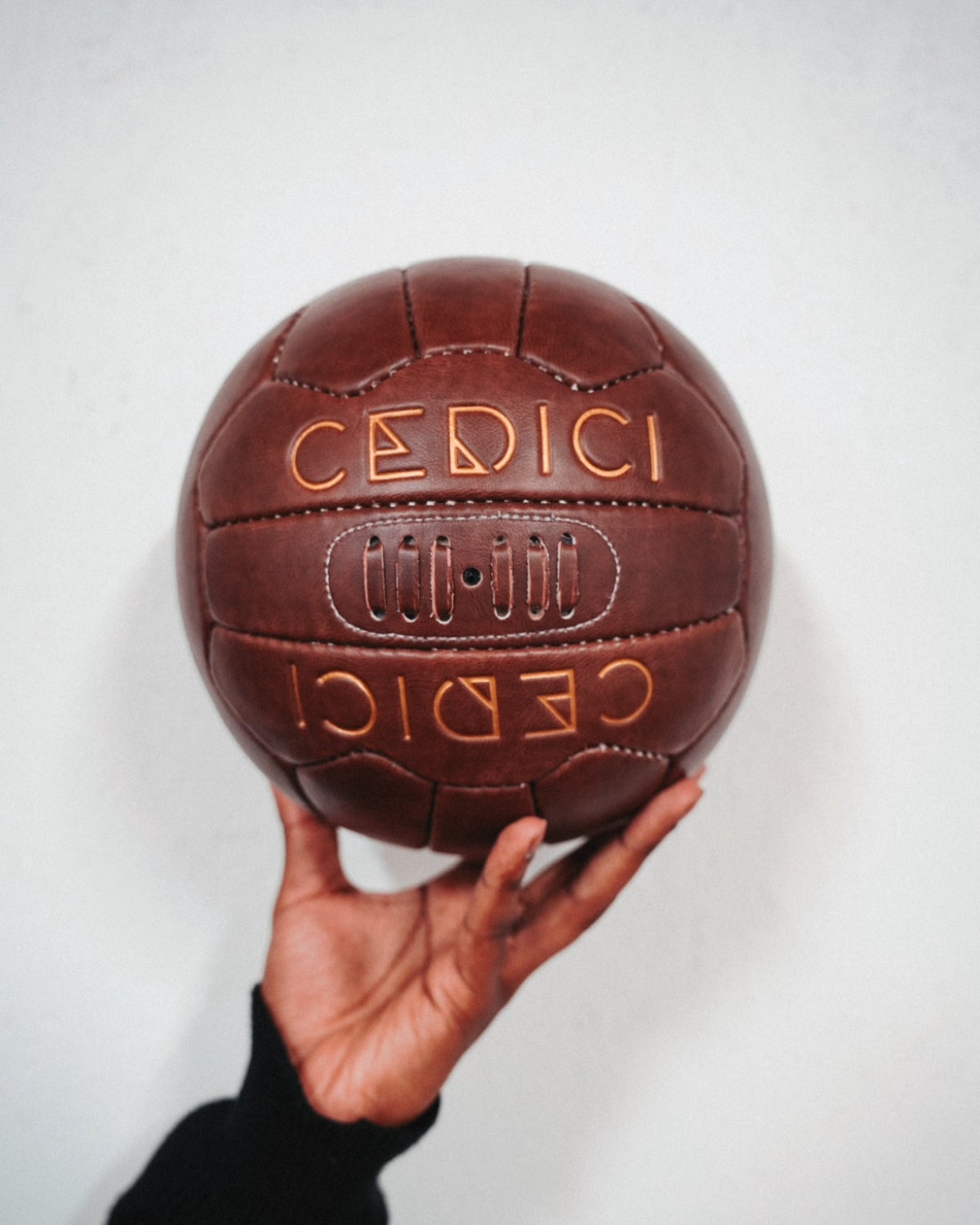 Hand holding a vintage-style brown leather football embossed with the CEDICI logo in gold lettering