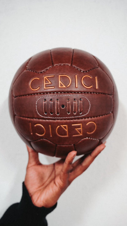 Hand holding a vintage-style brown leather football embossed with the CEDICI logo in gold lettering